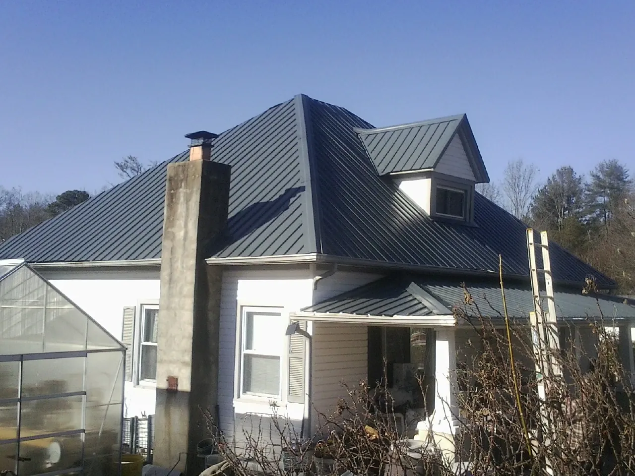 Dark blue standing seam metal roof on a white farmhouse with dormer — Slate & Tile Roof Repair by Roofing Brothers in Cody
