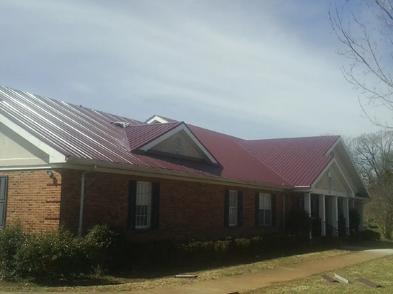 Red metal roof with gabled entries on a long brick building, from a Hail Damage Roof Repair job in Cody