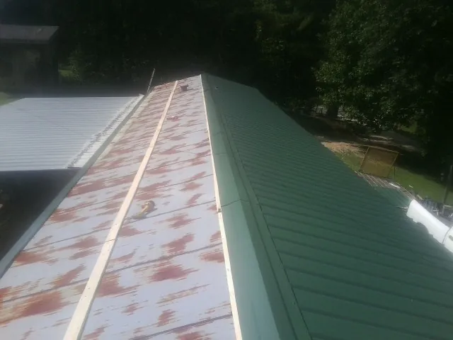 Old rusted panels beside newly installed green metal roofing — Wind Damage Roof Repair by Roofing Brothers in Cody