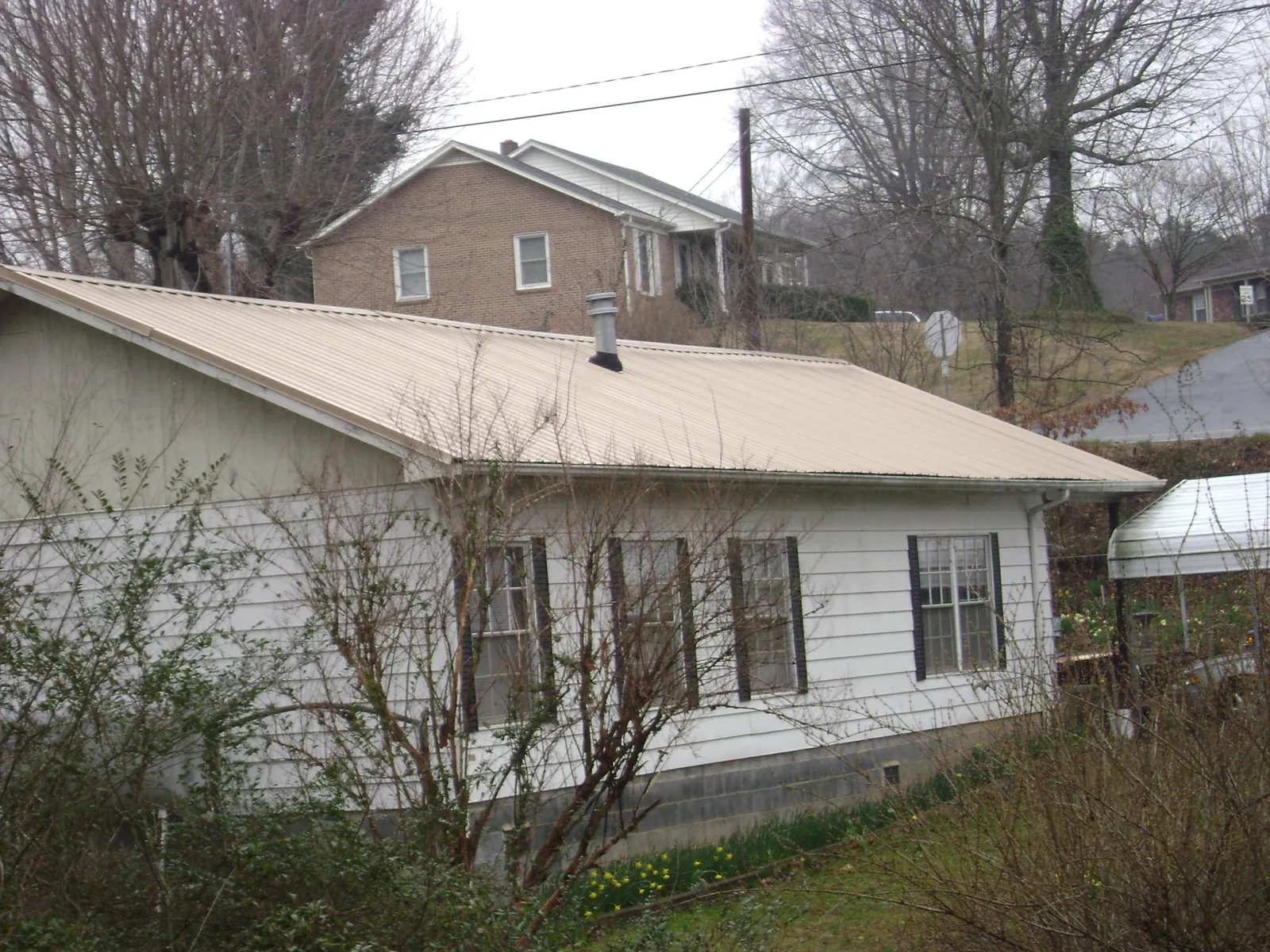Tan metal roof on a white sided house set into a hillside — Commercial Roofing by Roofing Brothers in Cody