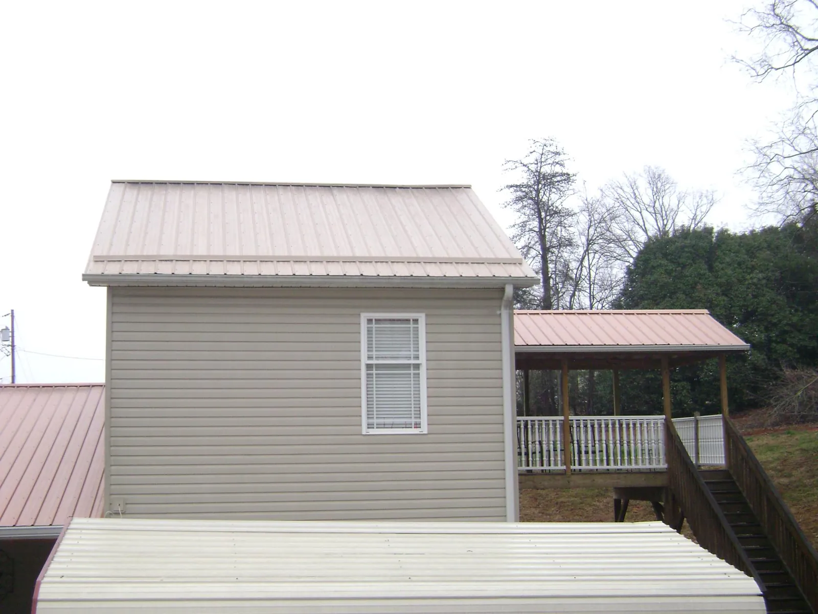 Tan metal roofs on a two story addition and attached porch, from a Roof Replacement job in Cody